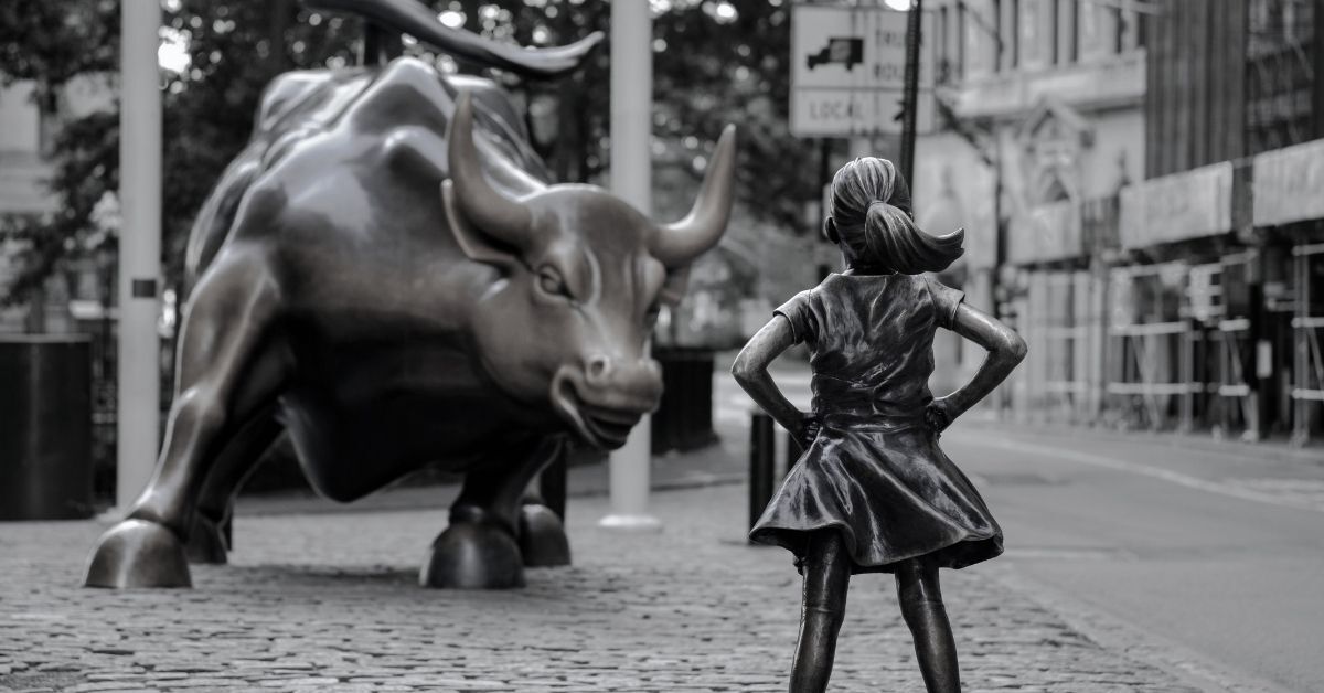 Black and white portrait of the Fearless Girl sculture opposite the Charging Bull sculpture in New York